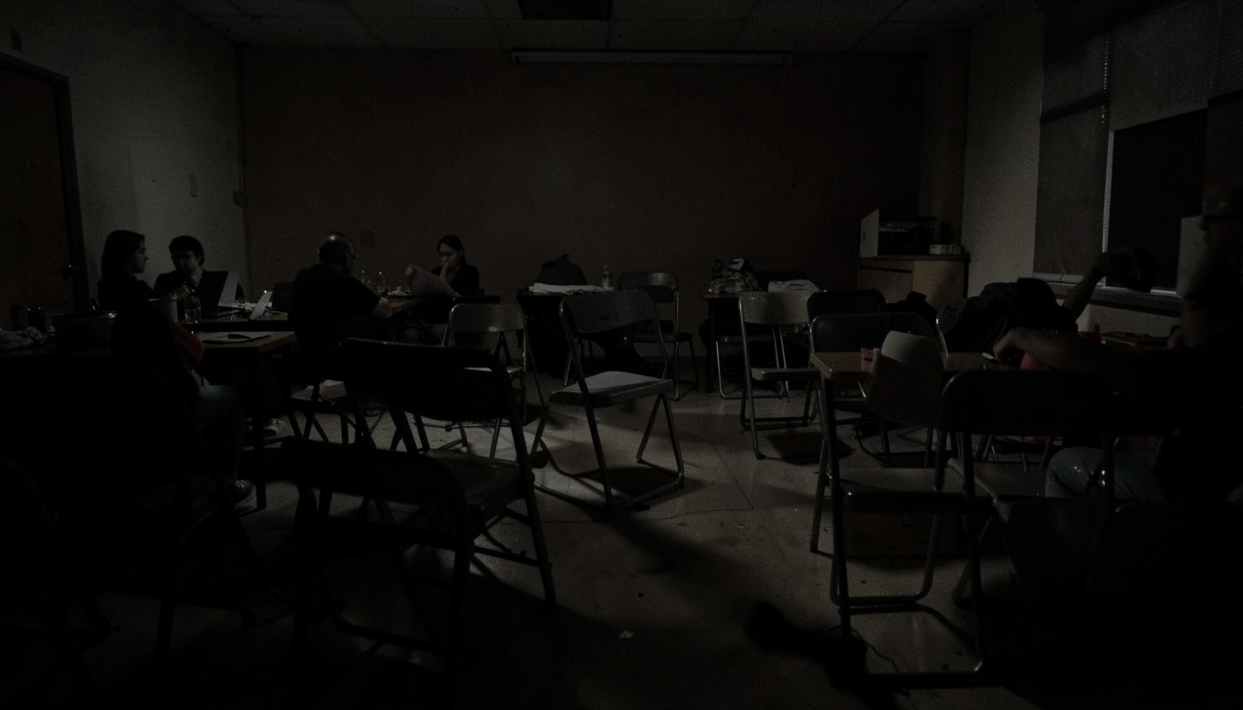 A dimly lit community gathering space with chairs arranged for a workshop, shadowy and calm atmosphere